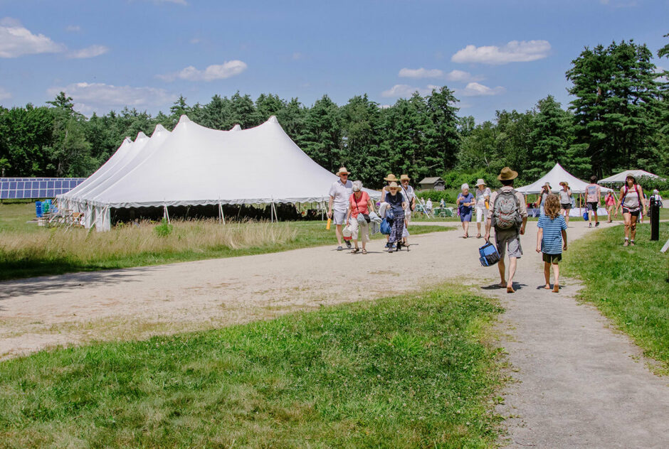Medal Day guests walk along dirt roads and pathways, making their ways throughout MacDowell's grounds. A large white tent is set up in the field, awaiting the start of the ceremony