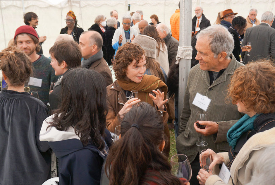 Fellows, supporters, and their friends stand in small groups and enjoy some cocktail-hour conversation during the New Hampshire Benefit in May 2022