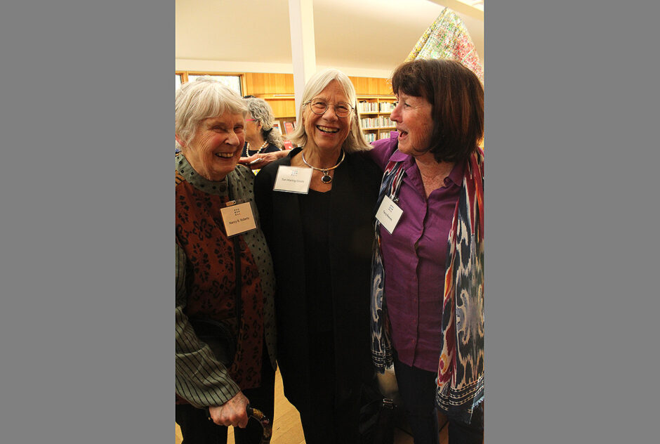 Three women laugh as they pose for a photo together inside the library. There are bookshelves behind them.