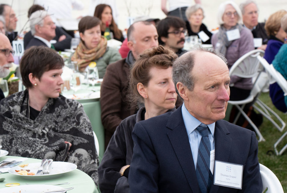 Fellows and supporters listen to the presentations while sitting at their tables during the New Hampshire Benefit in May 2022. They all face away from the camera, their eyes on the stage.