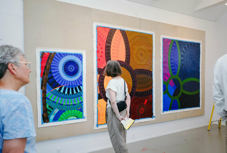 A woman stands and admires large, boldly colored paintings hung on a wall. Her hands are held neatly behind her back,