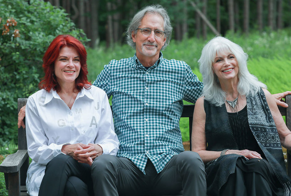 Roseanne Cash, John Leventhal and Emmylou Harris sitting together on a bench, smiling warmly