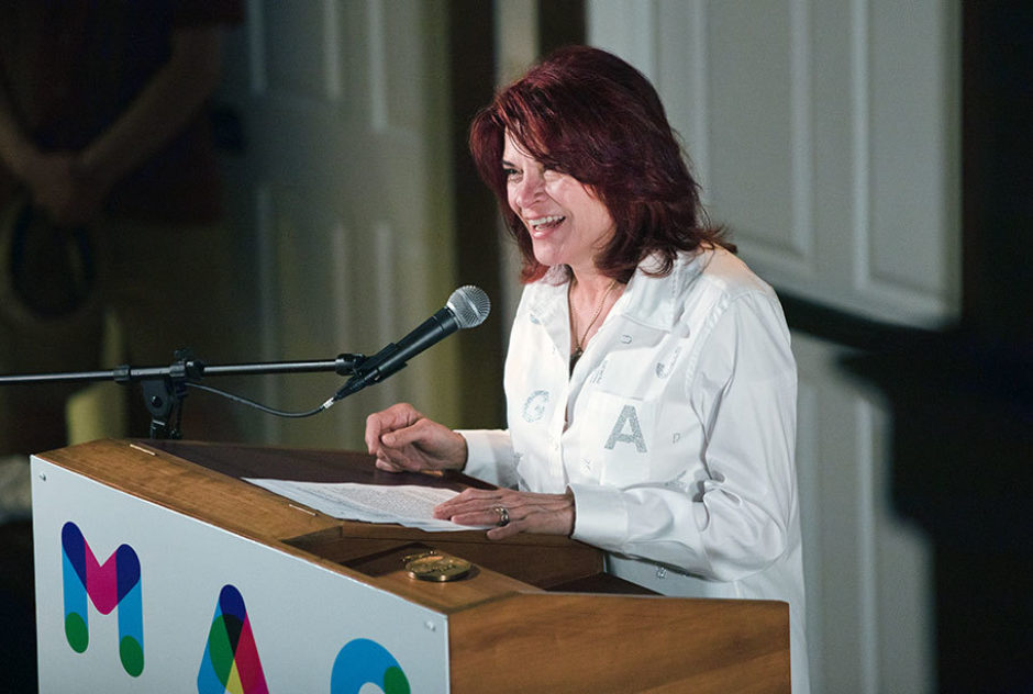 Roseanne Cash accepts her Medal with a speech. She stands at a podium and smiles brightly