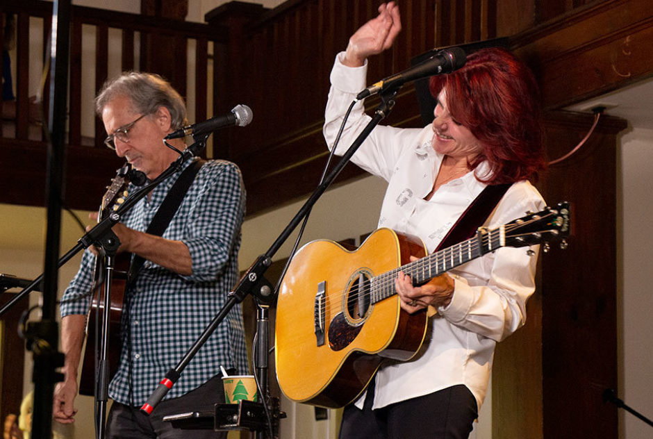 Roseanne Cash performs on stage with her husband John Leventhal. They are both playing the acoustic guitar.