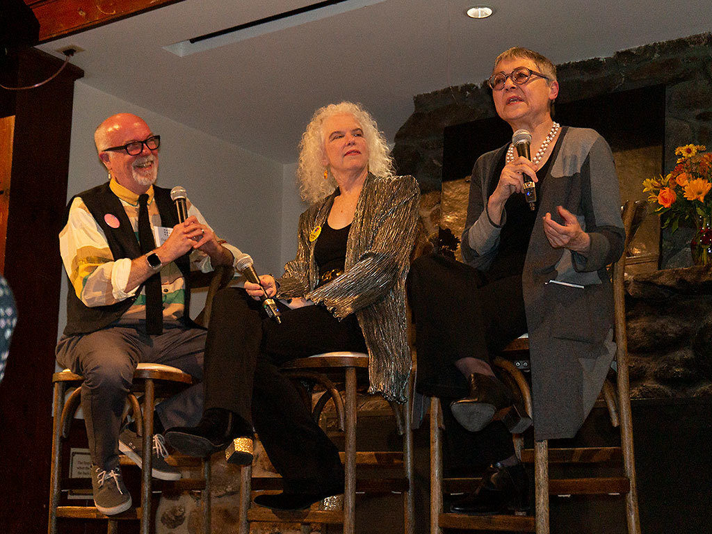 Fellows Dan Hurlin, Martha Mooke, and Sigrid Nunez sit on stools on a stage during a panel discussion at the 2019 New Hampshire Benefit.