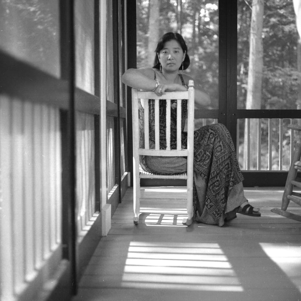 Katherine Min on the porch of Monday Music Studio in 1999. She sits in a white chair and hangs her arm over the back