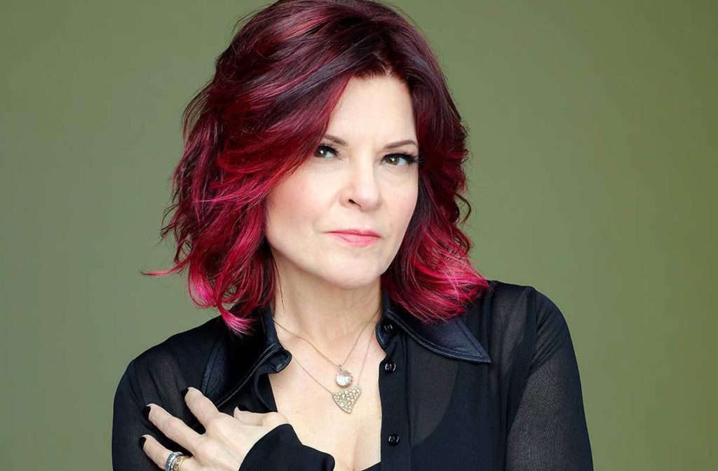 Portrait of Roseanne Cash. One of her hands rests on her should and she looks directly into the camera.