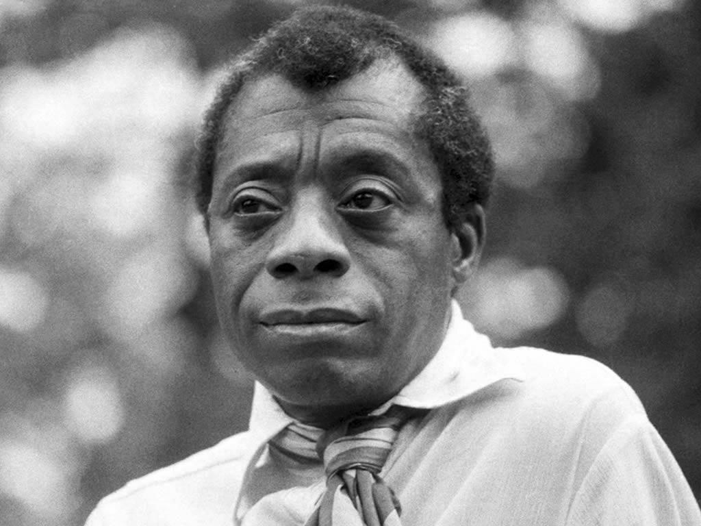 Black and white images of James Baldwin. He is wearing a white collared shirt and a tie.