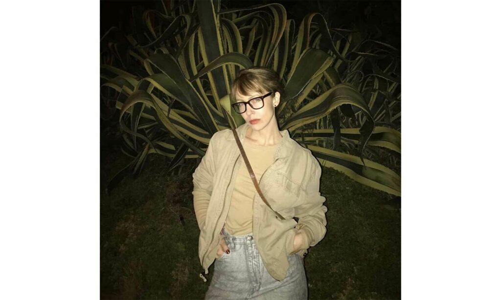 Night image of filmmaker Courtney Stephens standing in blue jeans and tan top and jacket with hands in pockets.