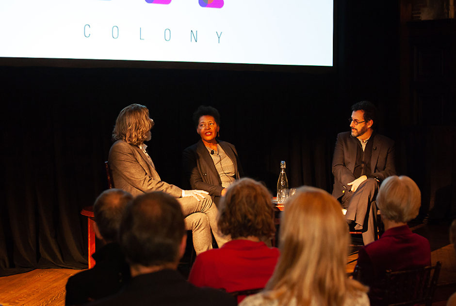 Three people sit in chairs on a stage for a panel discussion