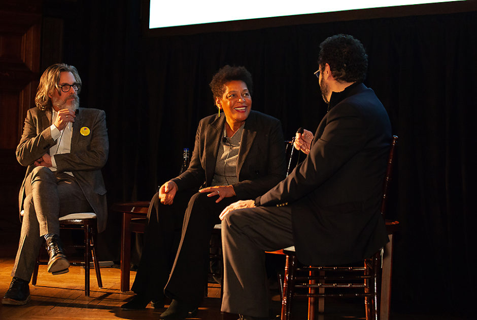 Three panelists sit in chairs on a stage for a discussion