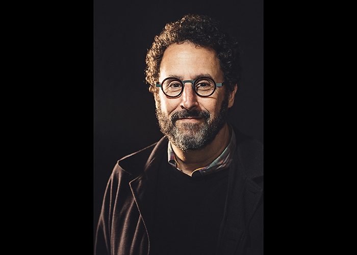 Portrait of Tony Kushner. He smiles softly and looks directly into the camera.