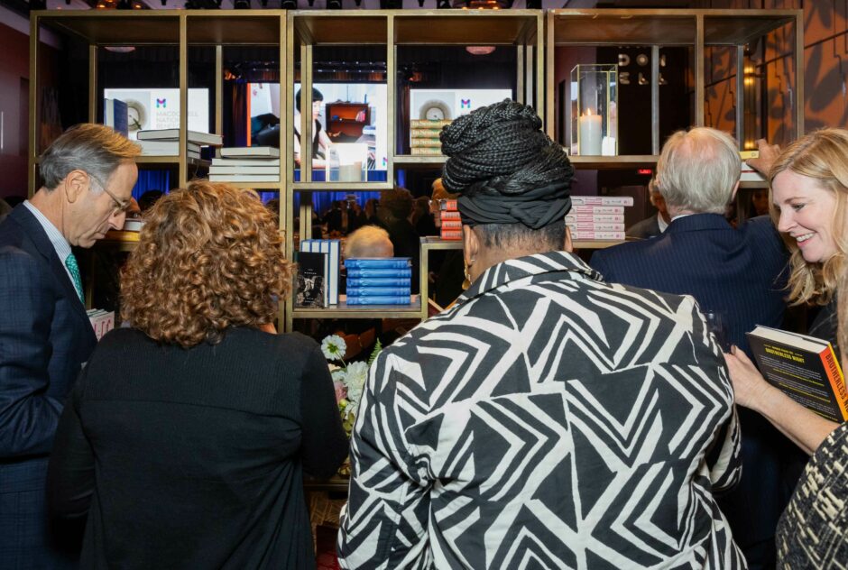 Several people with their backs towards the camera look at a gold bookcase with books