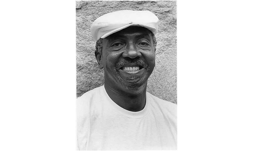 Portrait of Etheridge Knight. He is smiling and wearing a white hat