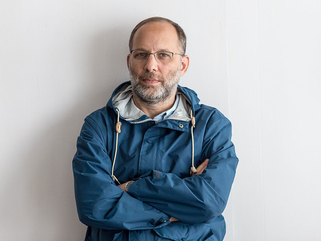 Portrait of Ira Sachs. He is wearing a blue hoodie and crossing his arms in front of him