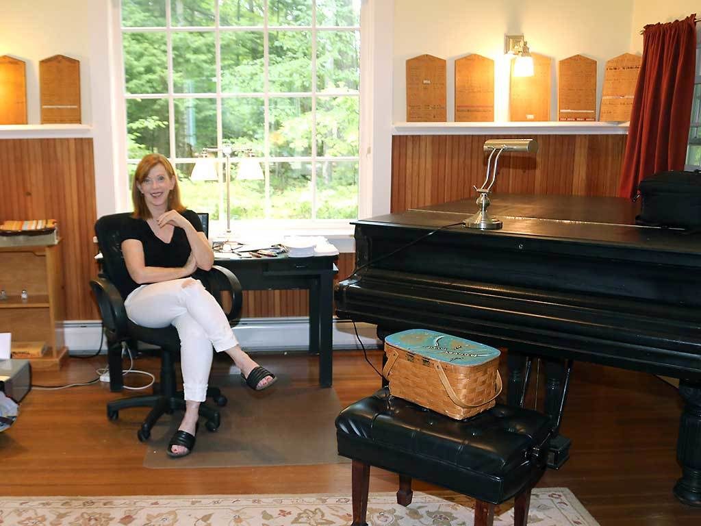 Portrait of Susan Orlean in her studio. She is sitting in a chair next to a piano.