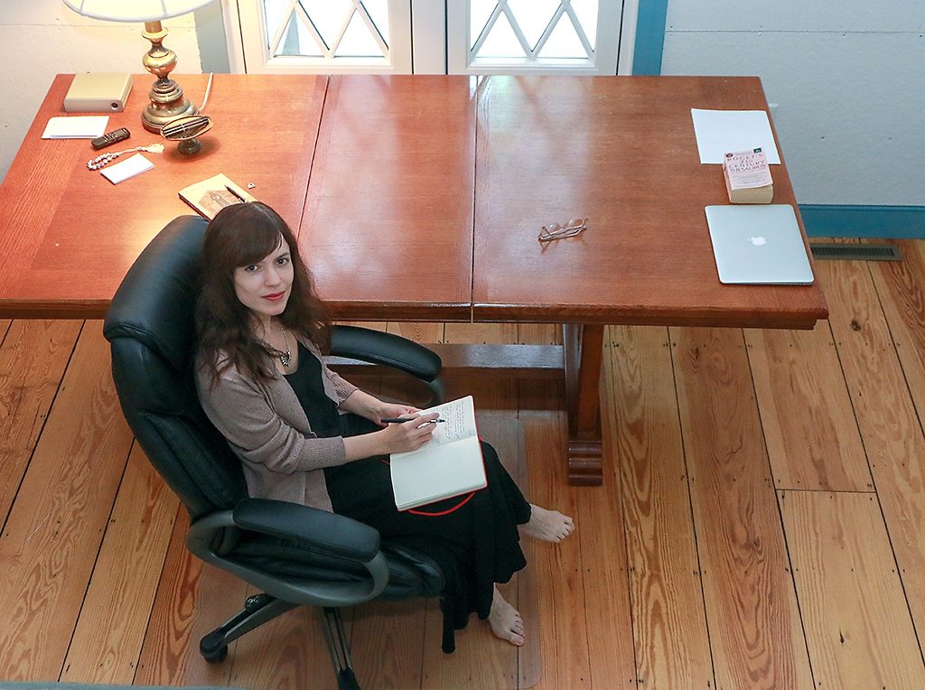 Fellow Alex Mar sitting at her desk in her studio. The image is taken from above, she has a pen in her hand and a notepad on her lap