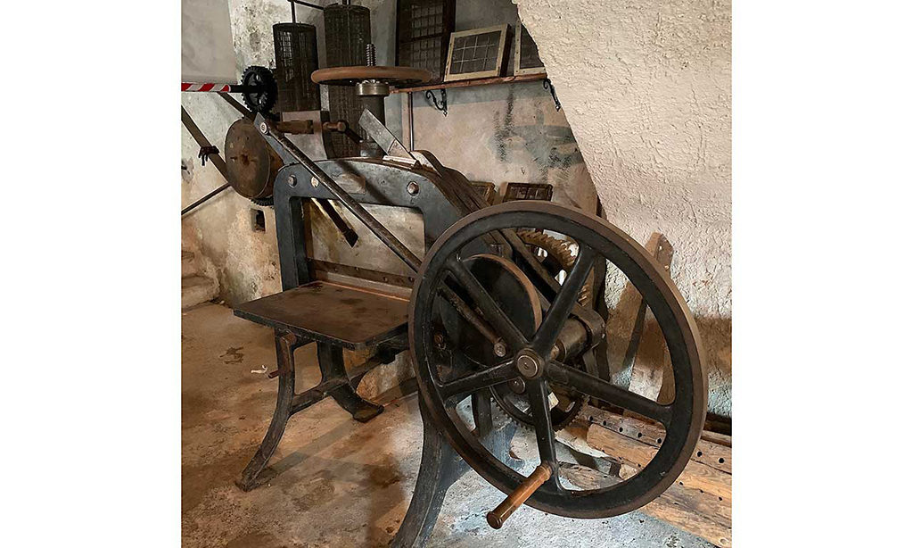 A parge, antique paper press. The machine features a large wheel and is made of a thick metal