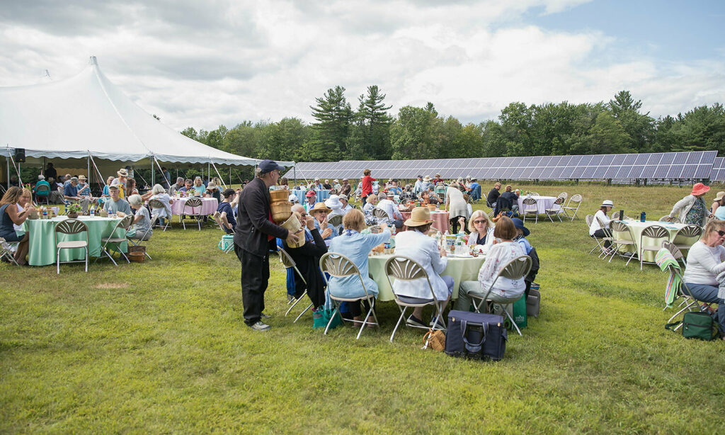 Many tables with picnickers gathered round are spread across a large field