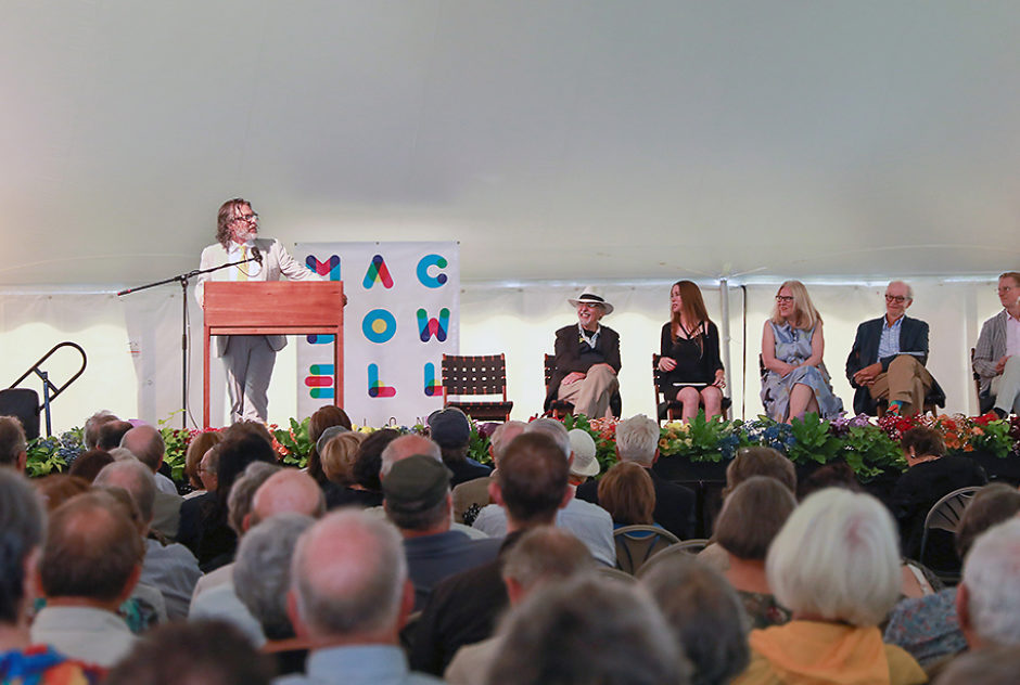 Michael Chabon stands at a podium, addressing the audience. To the right of him sit four people who will also speak during the ceremony. In the foreground, you can see the back of the heads of the audience who are there to see the ceremony.