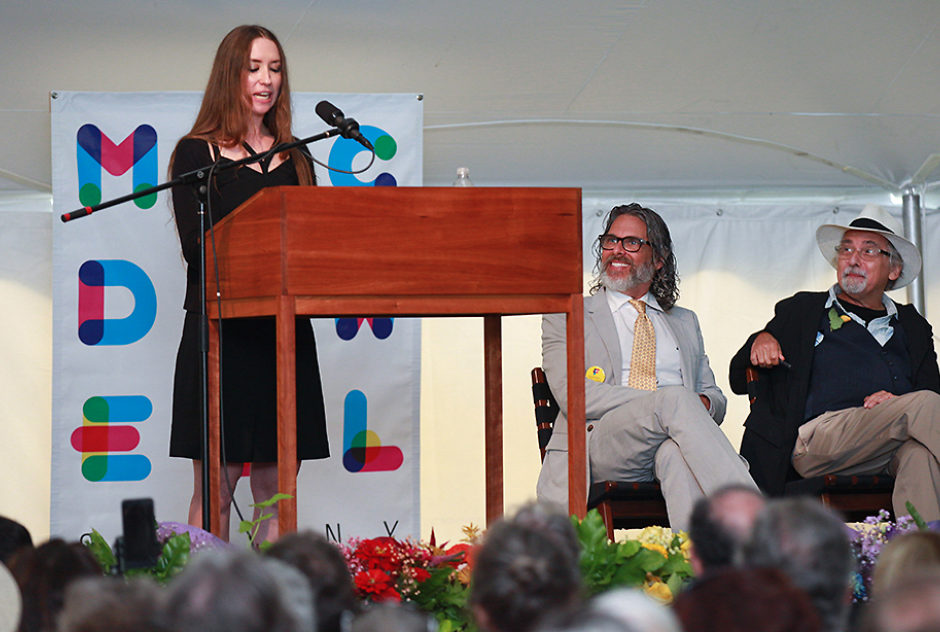 Hilary stands at the podium and speaks to the crowd. Next to her, sitting in a row of chairs is Michael Chabon and Art Spiegelman.