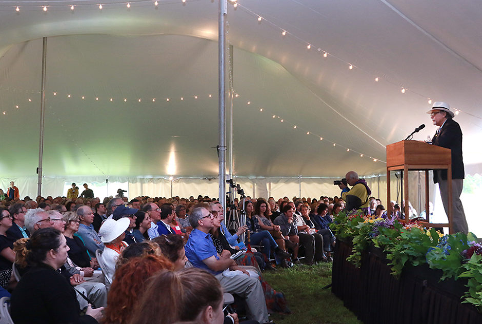 Art Spiegelman stands at the podium, addressing the crowd who look on from their seats under a large tent