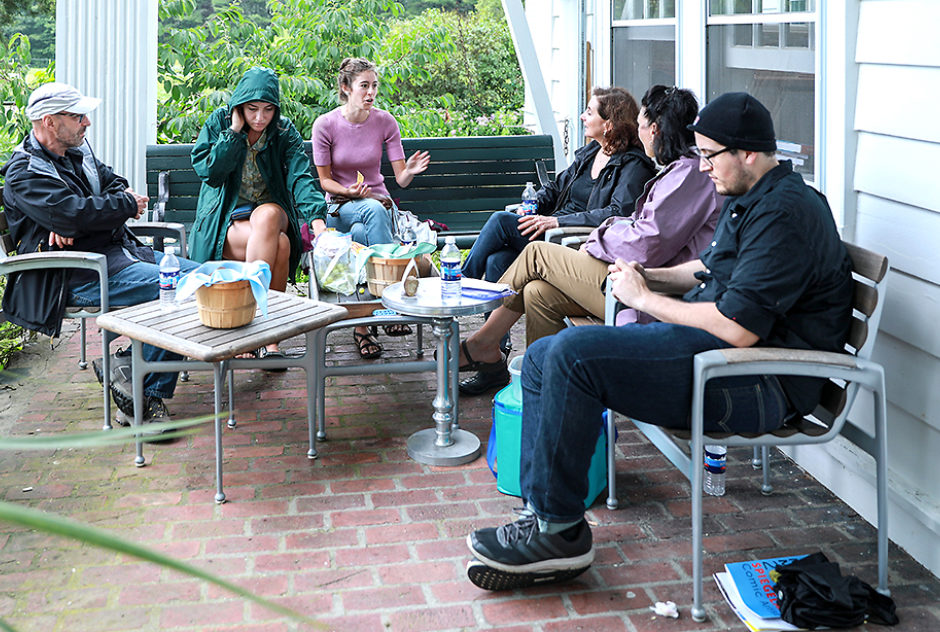 A group of people gather on a porch for conversation and a picnic