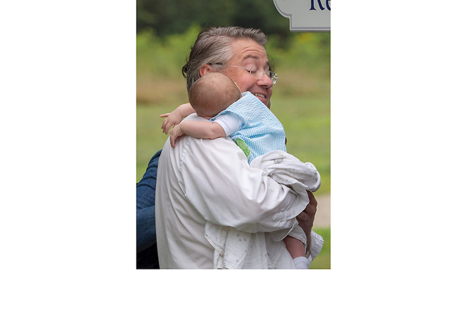 A man walks across the field, a sleepy infant rests their head on his shoulder