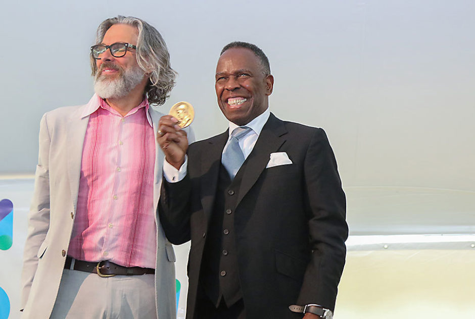 Michael Chabon stands next to Medal winner Charles Gaines who is holding up his medal and smiling widely.