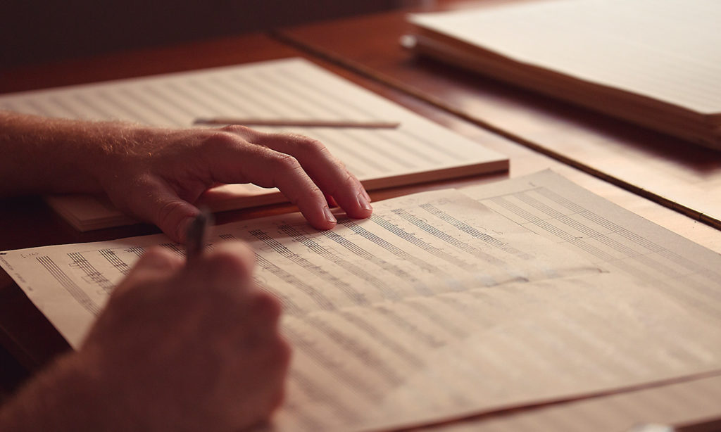 close up shot of a Fellows hands while they write music on score sheets