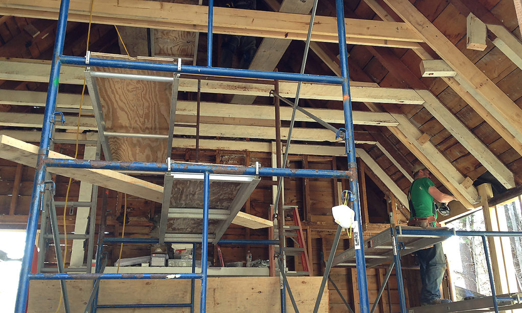 Interior of Delta Omicron studio renovation. There is scaffolding around the room and a builder works on installing the rafters