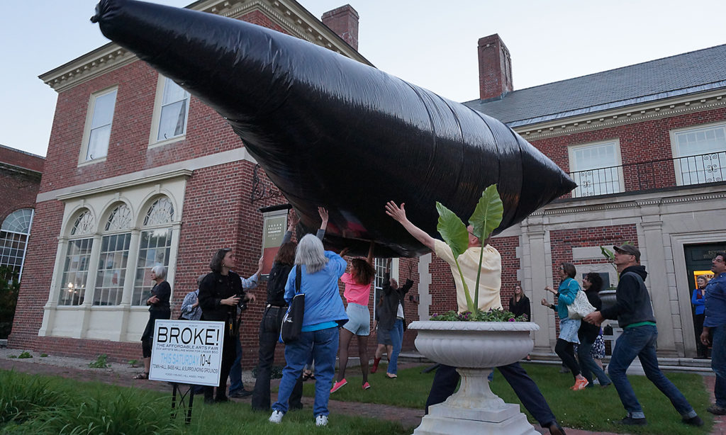 A group of people engage with a large, black, floating object outside of the Peterborough Historical Society