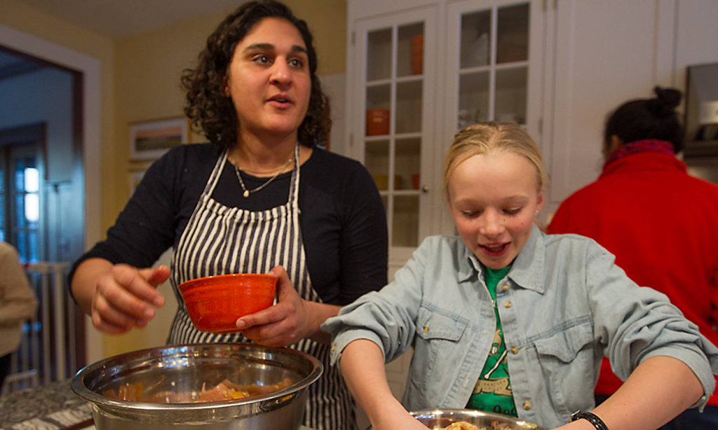 A woman and a little girl stand at a kitchen island and prepare food together