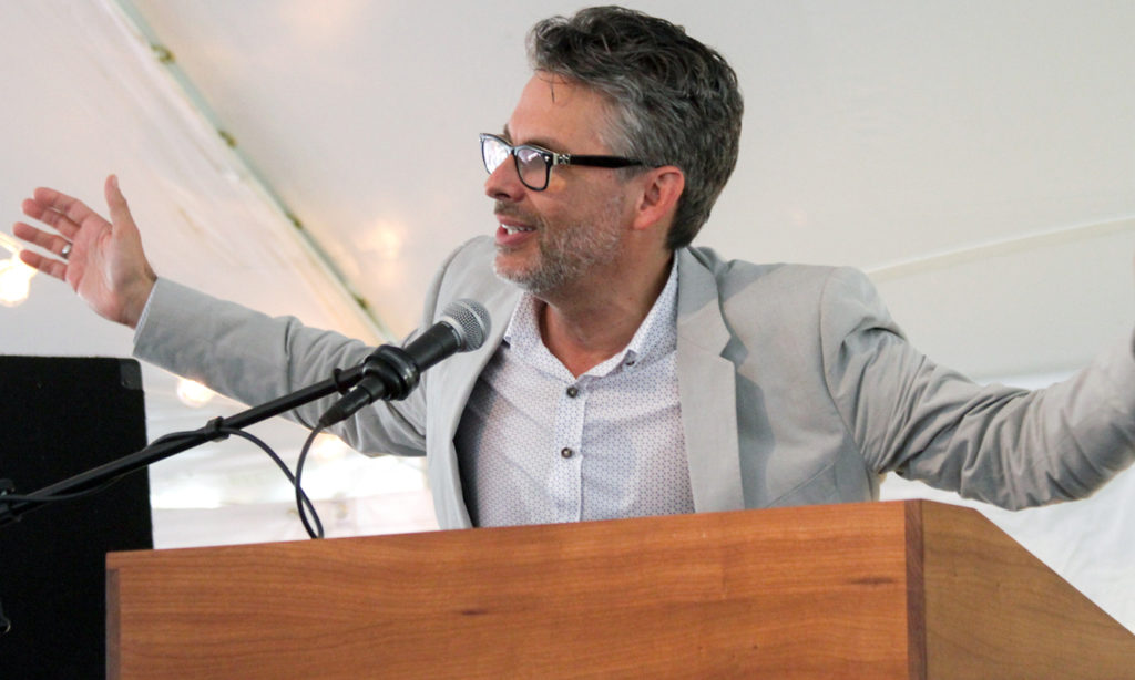 Michael Chabon speaks at a podium. He gestures with his arms are spread wide
