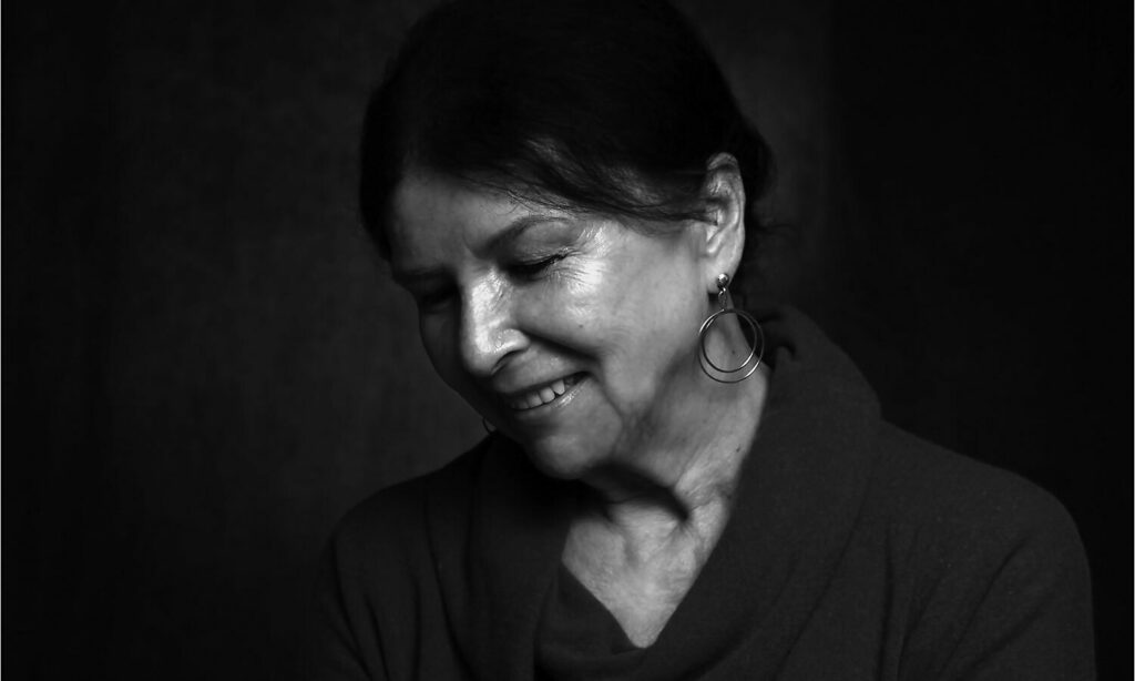 Alanis Obomsawin smiling slightly and gazing down in black and white