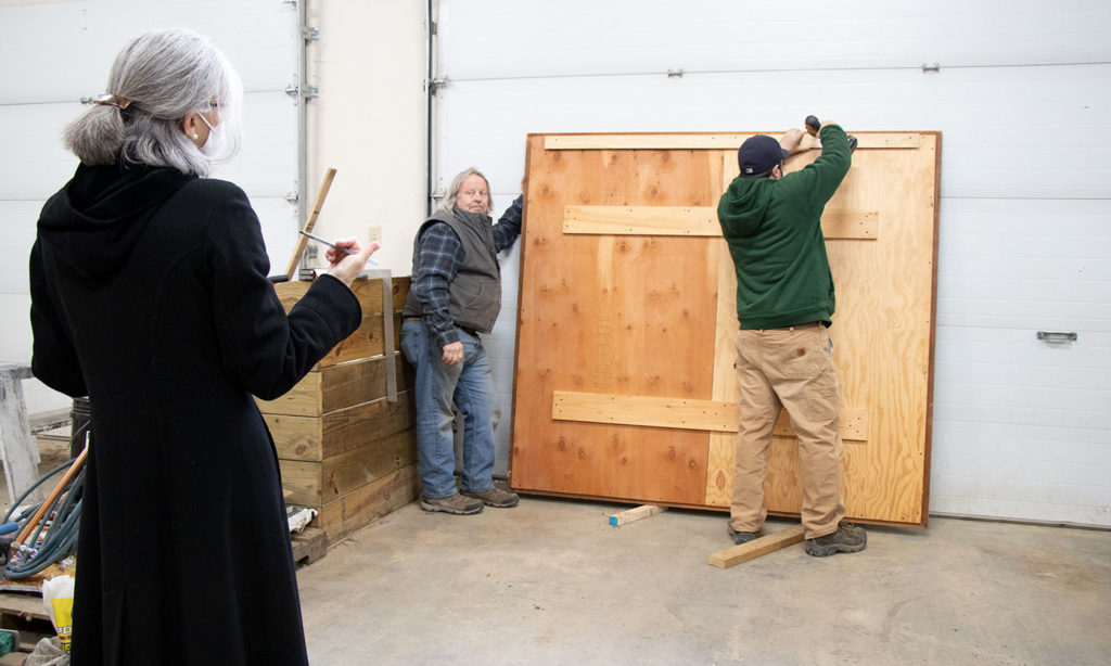 J-Crew's Jamie Sargent attaches a hanging bracket to the back of the frame as Colette Lucas and Maintenance Foreman John Sieswerda talk about the work's history. 
