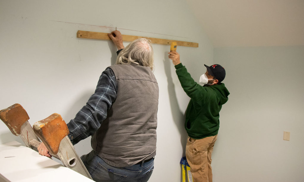 J-Crew levels the hanging bracket on the wall in the main hall to receive the large painting.