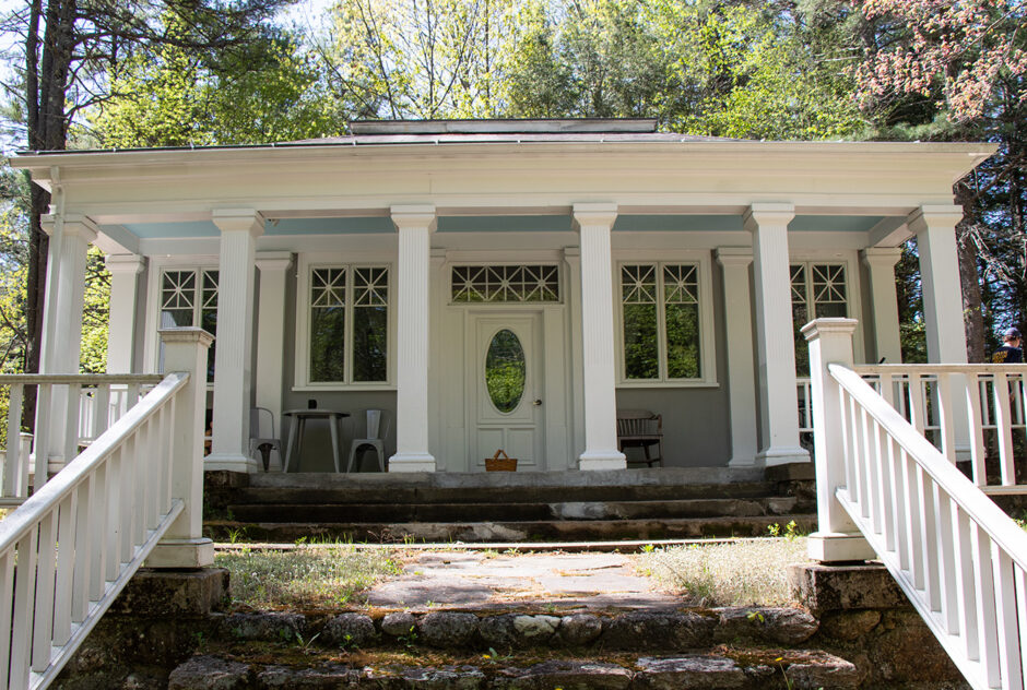 Watson studio in the spring. Large stone steps lead up to the building, which has large white columns lining the front porch. The trees surrounding the studio are beginning to leaf-out and the sun is shining brightly.