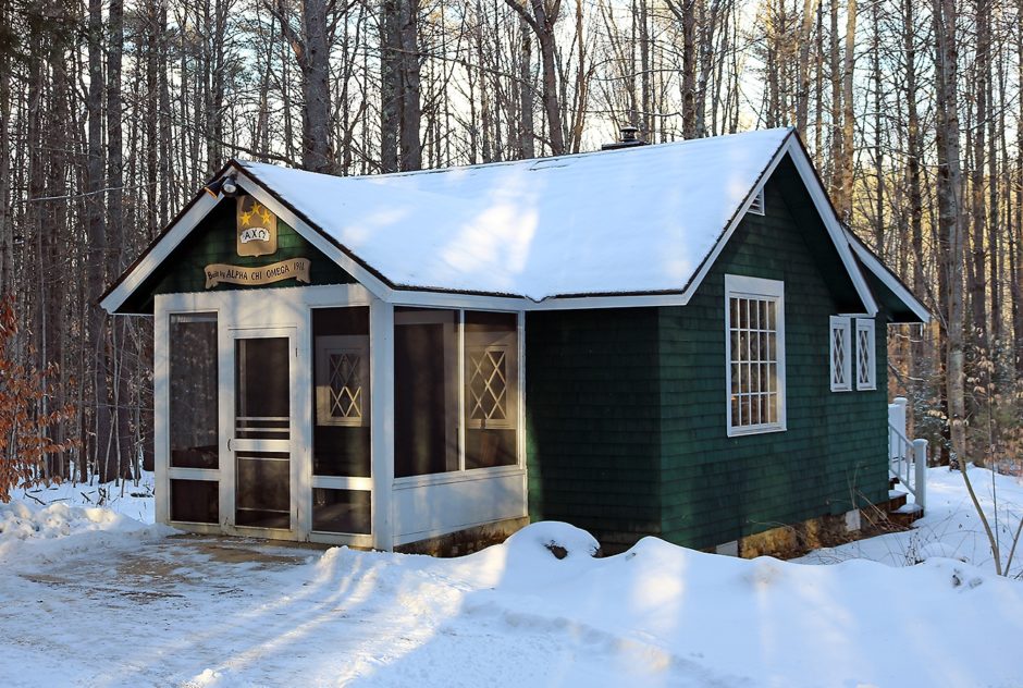 Star Studio in winter surrounded by snow. The small green building sits in a dense forest. The setting sun casts warm light on the front porch.