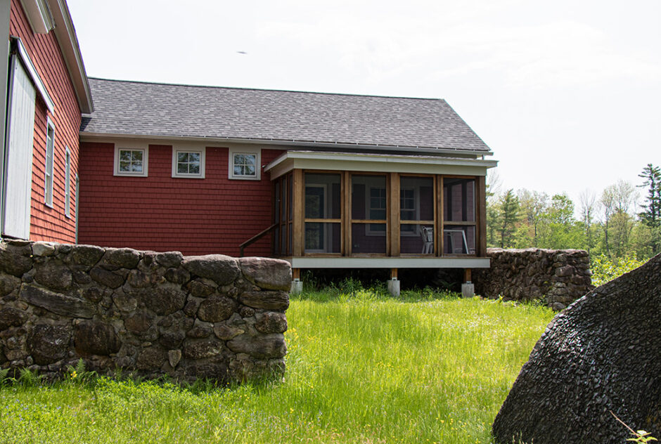 Back side of Eastman studio in spring time. The red building, attached to a large barn, has a screen porch and looks out to a grassy courtyard.