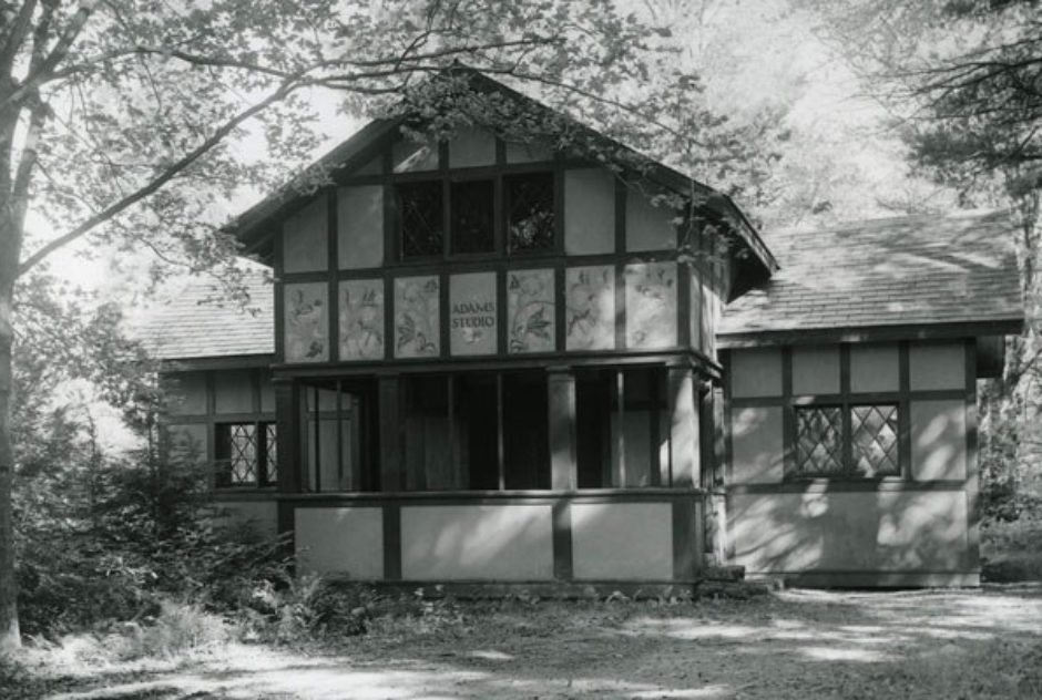 Black and white image of Adams Studio in summer. Speckled light falls on the building as it filters through the trees