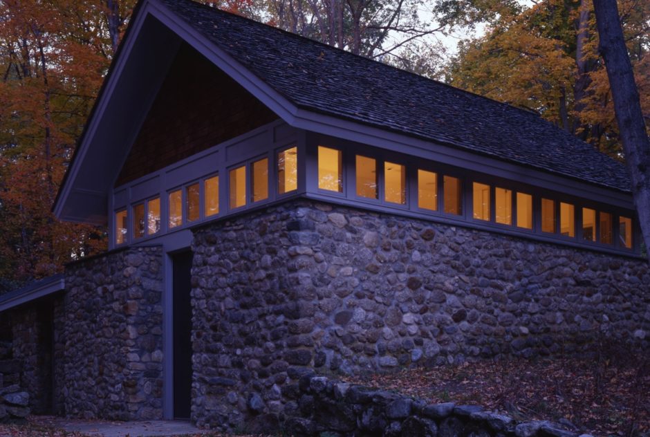 Heinz Studio at dusk in the fall. The stone building features a a row of small windows that wrap around the top of the walls, just under the roof. A warm light emanates from these windows.
