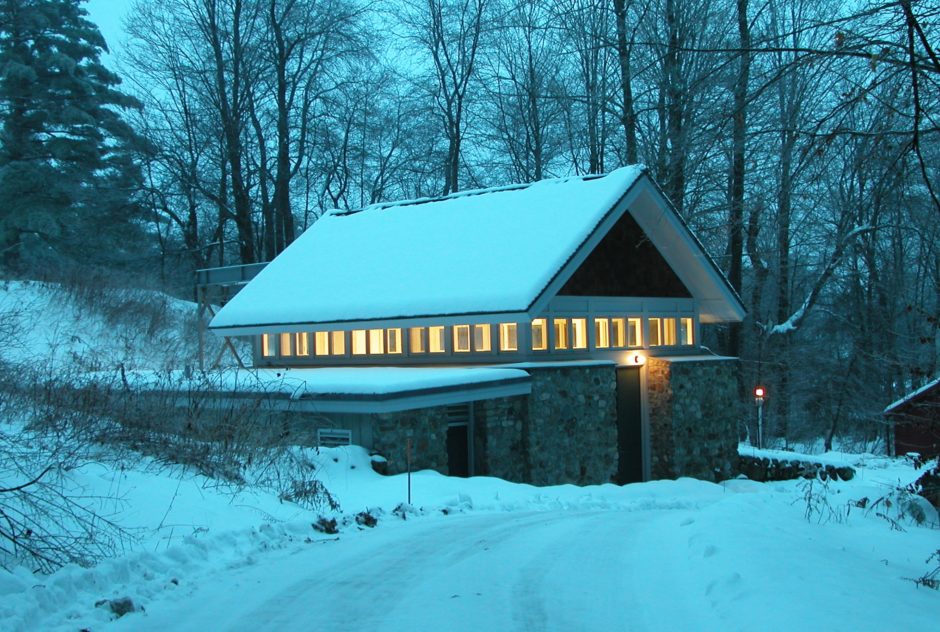 Heinz Studio on a snowy, winter evening. The late evening light cast a shade of blue on the scene. The row of windows along the roof line are illuminated from the warm light inside.