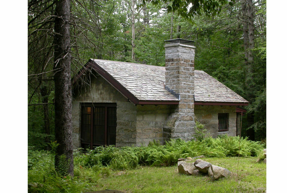 Mixter Studio in summer surrounded by lush green forest and ferns. The small stone studio is nestled into the forest and cloudy weather casts a gray light on the scene.