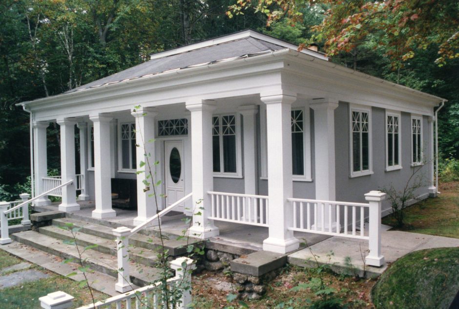 Watson Studio in early fall. The grey building, featuring six while columns along its porch, has a stone staircase leading to a small courtyard. The studio is nestled into a dense forest.