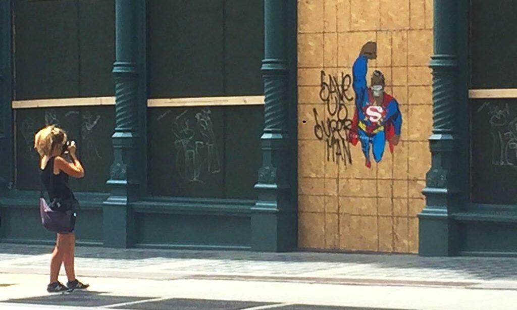 woman in Soho New York City takes photo of graffiti of superman flying with words: save us superman